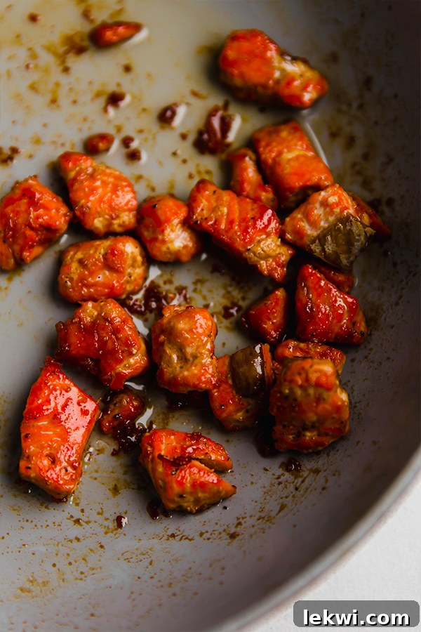 A close-up shot of cubed salmon being cooked in a large skillet, glistening with the vibrant firecracker sauce. The salmon pieces are evenly coated, suggesting a flavorful and well-prepared dish.