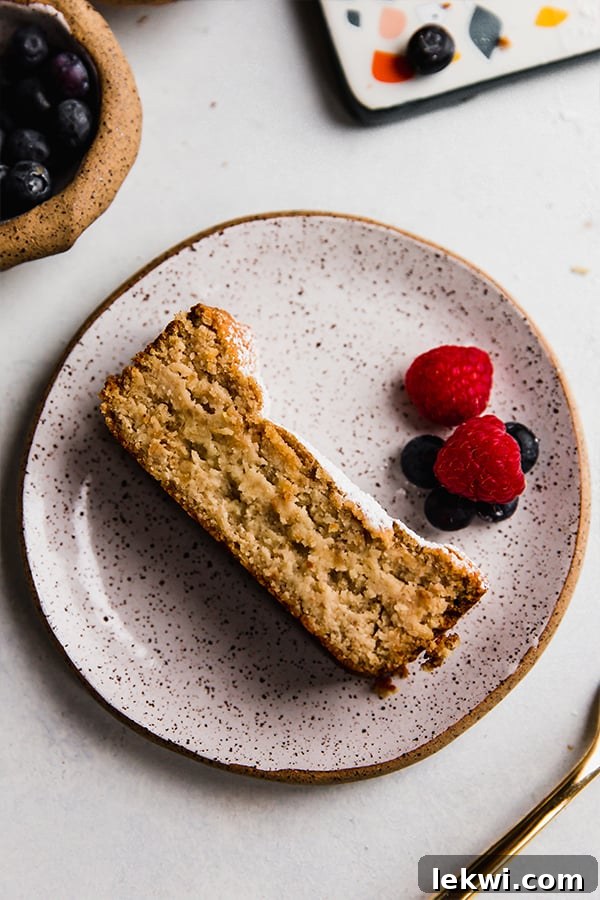 A beautifully sliced piece of paleo pound cake on a white plate, garnished with fresh berries.