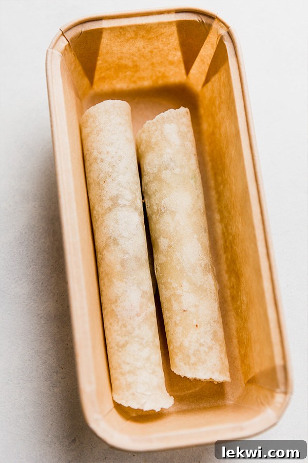 A container holding two perfectly rolled, uncooked sweet potato and beef taquitos, showcasing their readiness for baking or freezing.