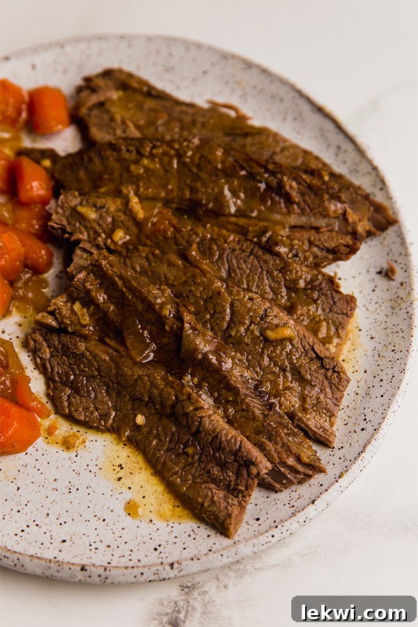 A generous serving of sliced brisket, roasted carrots, and onions on a white plate, garnished with fresh parsley.