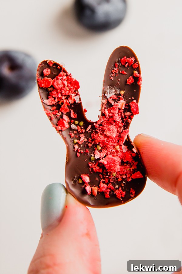 A single, perfectly crafted dairy-free chocolate Easter bunny, delicately held between fingers, showcasing its smooth texture and strawberry topping, ready to be enjoyed.