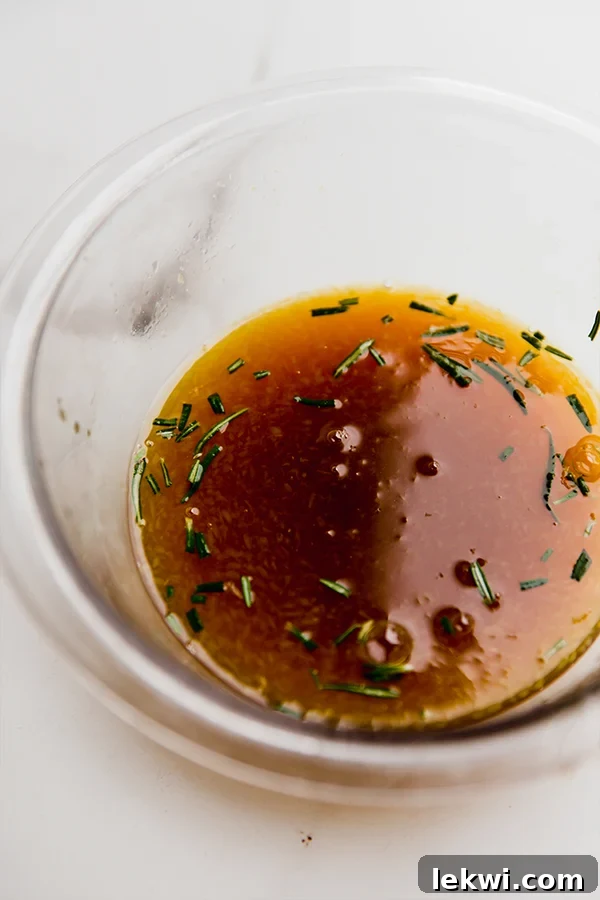 A close-up shot of a glass bowl holding a vibrant orange-colored marinade, with visible flecks of fresh rosemary, ready to infuse flavor into the chicken.