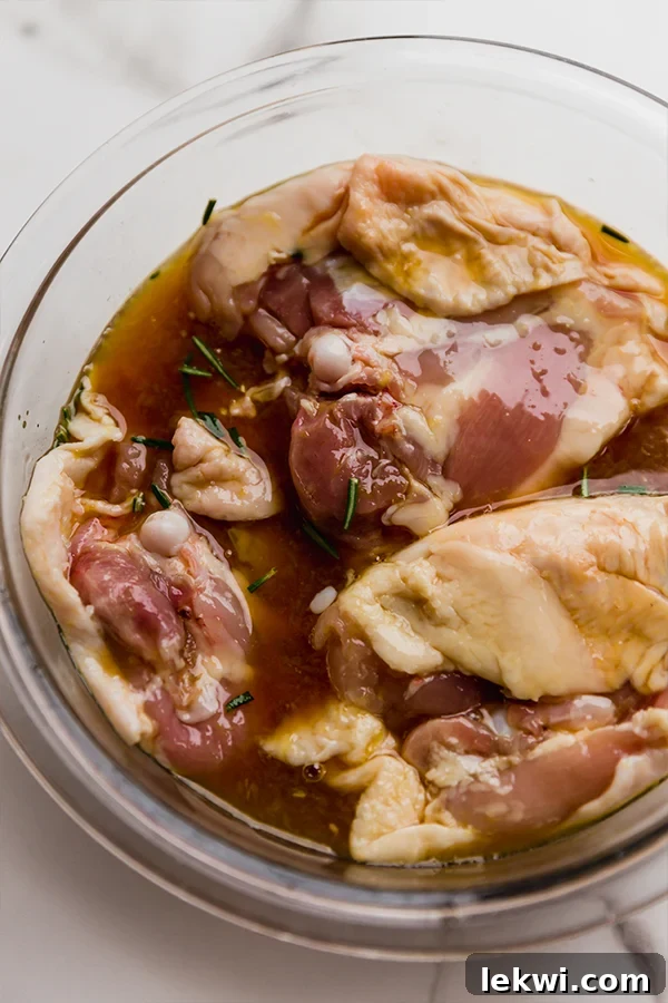 Chicken thighs submerged in a vibrant orange marinade in a clear glass bowl, glistening and absorbing the flavors.