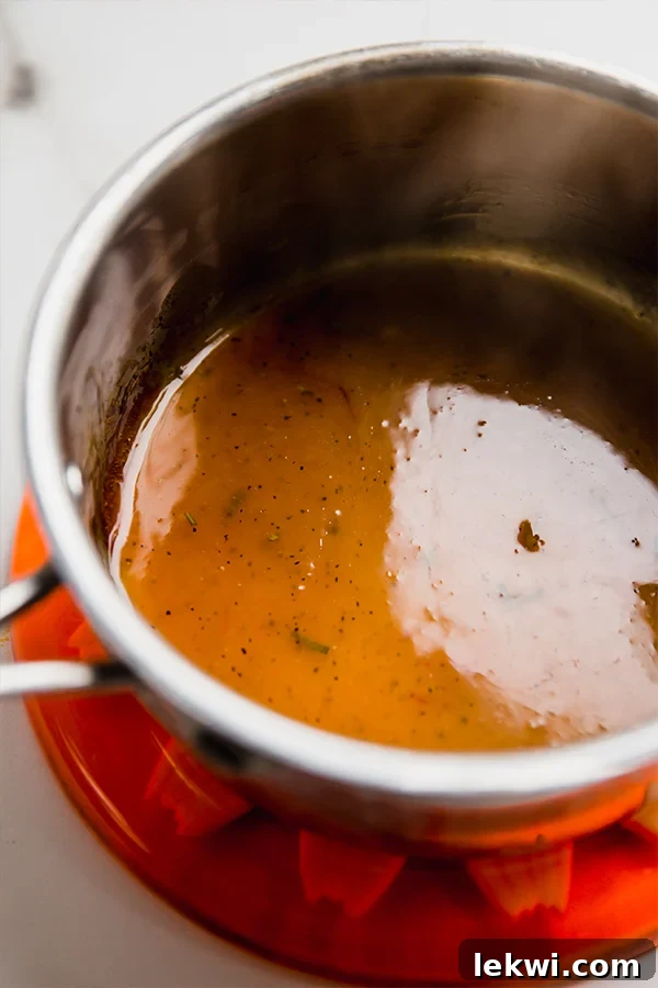 A small saucepan on a stovetop, containing a simmering, golden-orange glaze, with a whisk stirring gently, creating a smooth and thick consistency.