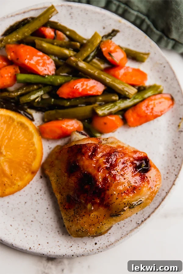 A beautifully plated dish featuring tender citrus glazed chicken thighs, vibrant green asparagus, sweet roasted carrots, and caramelized orange slices, ready to be enjoyed.