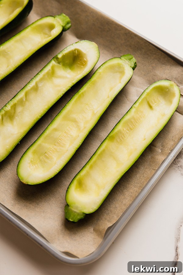 Hollowed-out zucchini halves arranged neatly on a baking sheet, glistening lightly with oil, and perfectly ready for the savory filling.