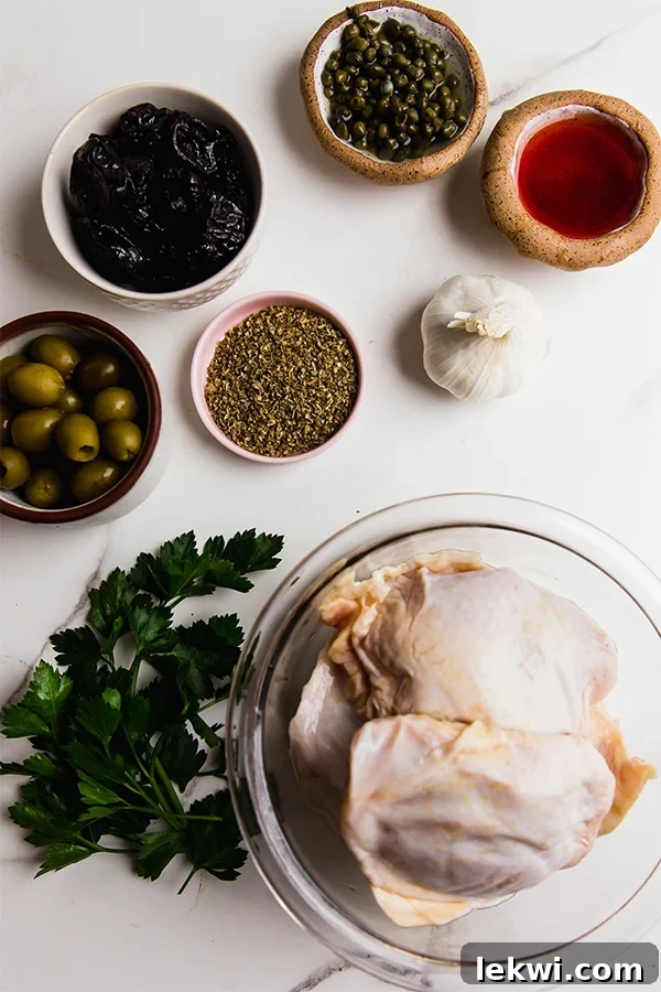 A vibrant collection of ingredients for Chicken Marbella, including bone-in chicken thighs, green olives, prunes, capers, olive oil, red wine vinegar, and fresh herbs, arranged on a rustic wooden board.