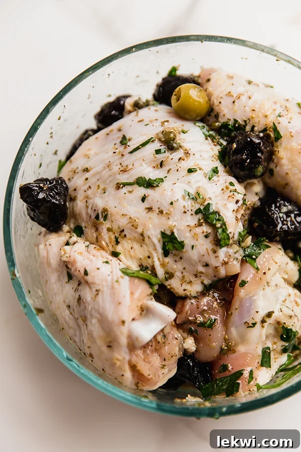 Raw chicken thighs coated in the vibrant marinade with olives, capers, prunes, and herbs, ready for cooking.