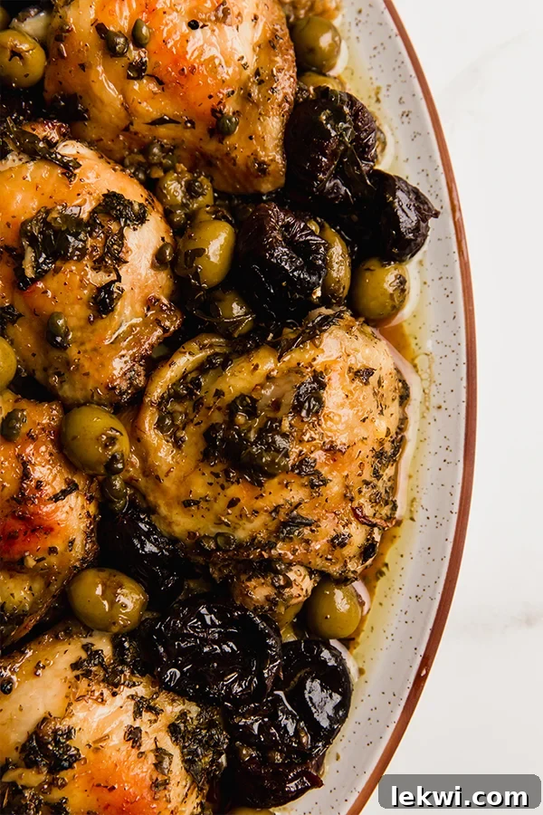Finished Chicken Marbella, beautifully arranged on a serving platter, garnished with fresh herbs, and surrounded by its rich, savory-sweet sauce, olives, and prunes.