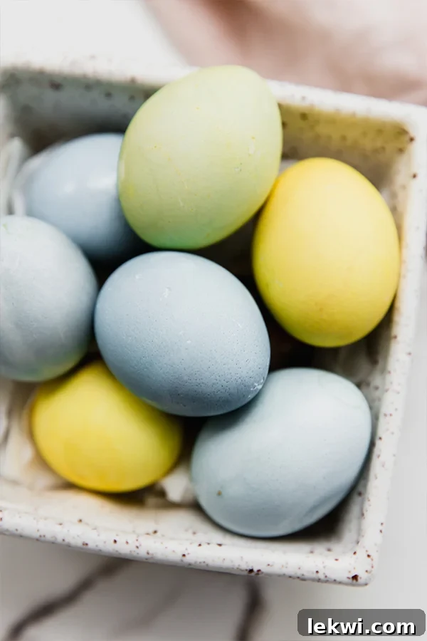 Collection of naturally dyed Easter eggs arranged beautifully in a vintage egg carton, showcasing shades of blue, yellow, and green.