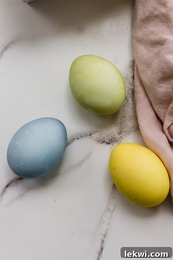 Three naturally dyed Easter eggs in vibrant blue, sunny yellow, and lush green, resting on a rustic wooden surface.