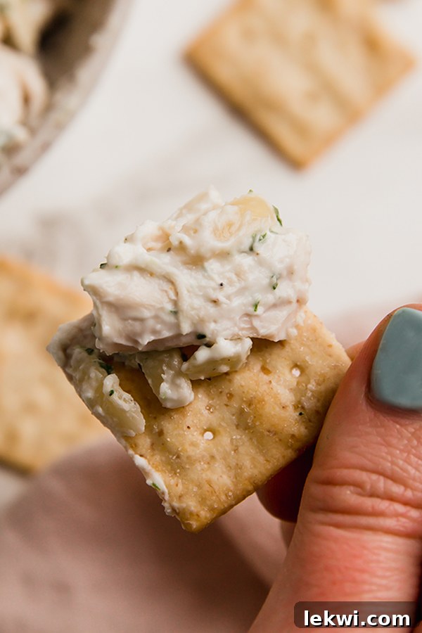 A perfectly crisp cracker, generously topped with creamy and aromatic tarragon chicken salad, showcasing its delicious texture and appeal.
