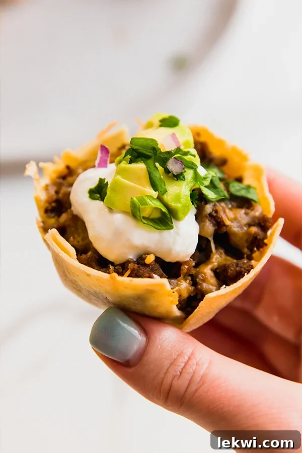 Person holding a loaded mini taco cup, showcasing its crispy shell and generous fillings.