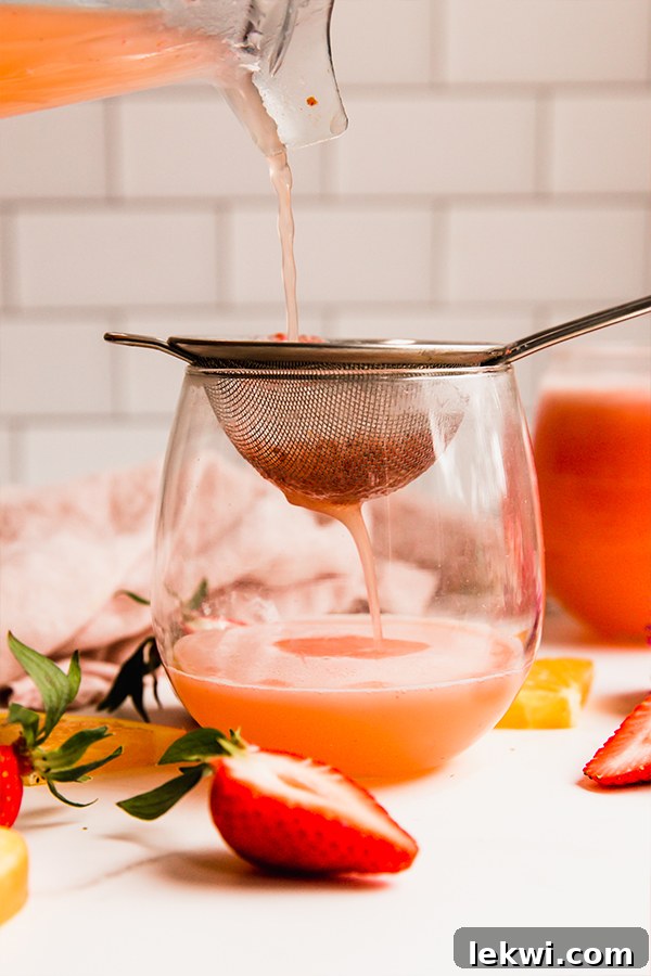 Straining the strawberry mimosa mocktail into a glass.