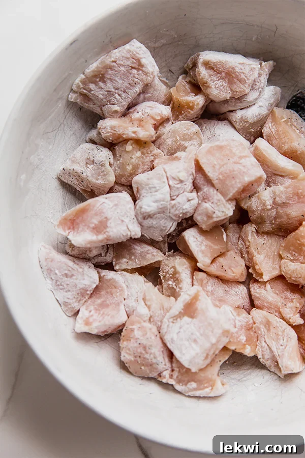 Cubed chicken breast coated in arrowroot starch, ready for cooking in a bowl.