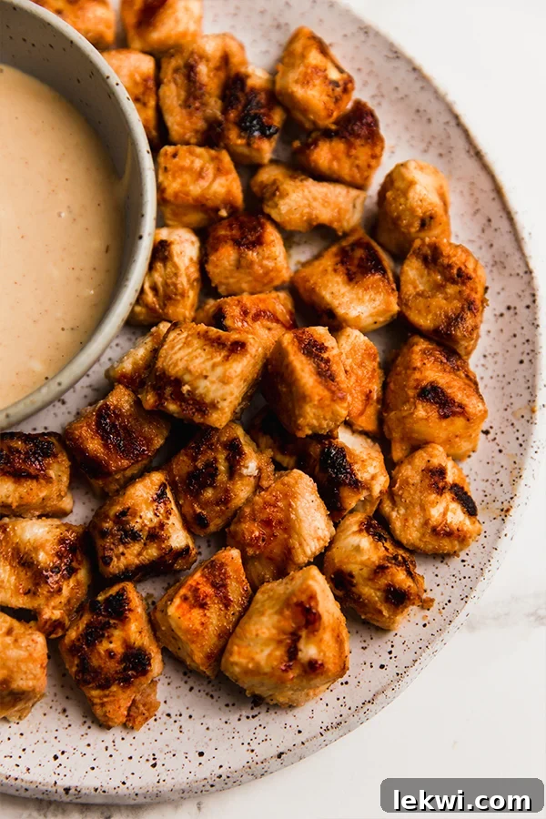 Copycat grilled Chick-Fil-A nuggets on a plate with a bowl of sauce, garnished with fresh herbs.