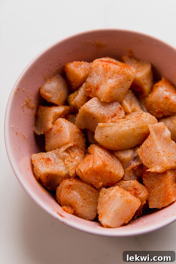 Cubed chicken breast marinating in a bowl with spices and vinegar.