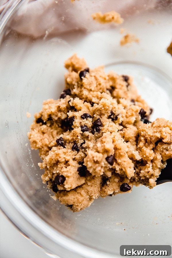 A close-up shot of the raw chocolate chip cookie dough in a mixing bowl, showing the texture and distribution of chocolate chips.