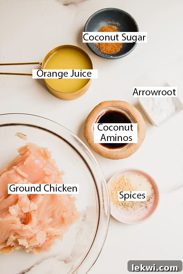 A collection of fresh ingredients laid out on a table, including oranges, ground chicken, spices, and bottles of sauce, ready for making orange chicken meatballs.