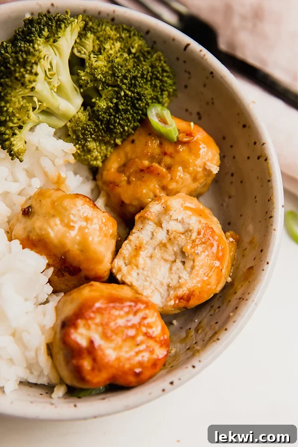 A serving bowl filled with orange chicken meatballs, accompanied by fluffy white rice and vibrant green broccoli florets, showcasing a complete meal.