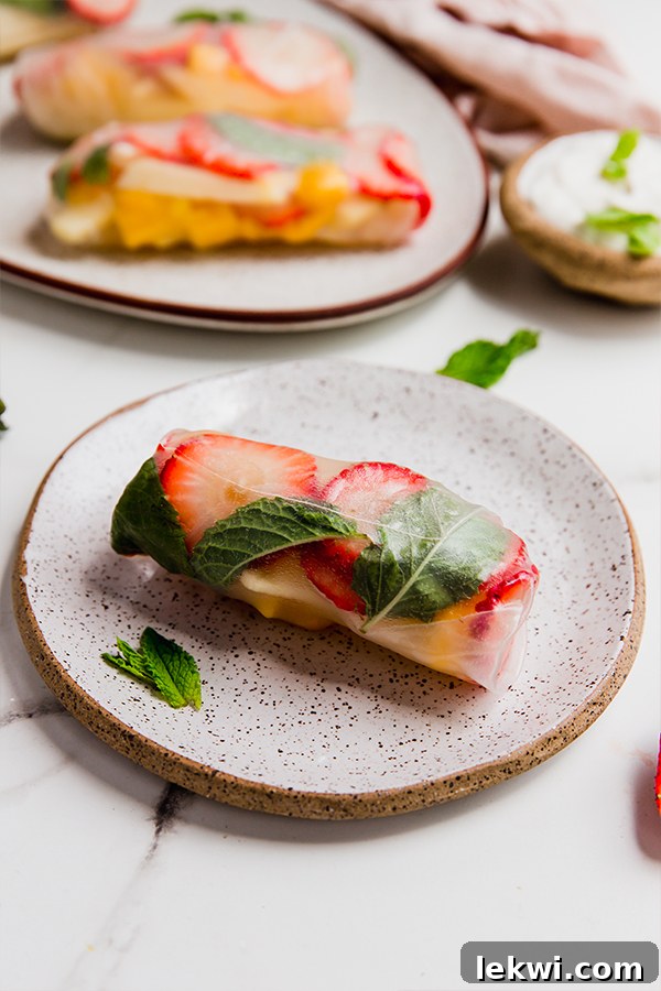 A single fruit spring roll, beautifully arranged on a plate with fresh mint leaves, showcasing its vibrant contents.