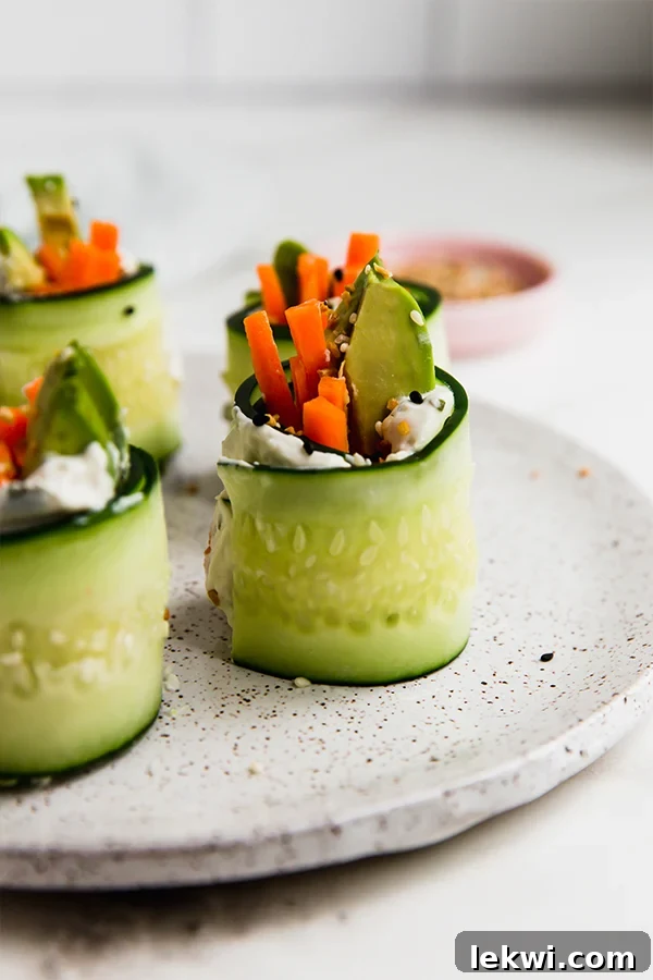 Smoked salmon bagel cucumber rolls standing up on a plate. This image shows beautifully arranged cucumber rolls filled with smoked salmon, cream cheese, avocado, and carrot, sprinkled with bagel seasoning, ready to be served.