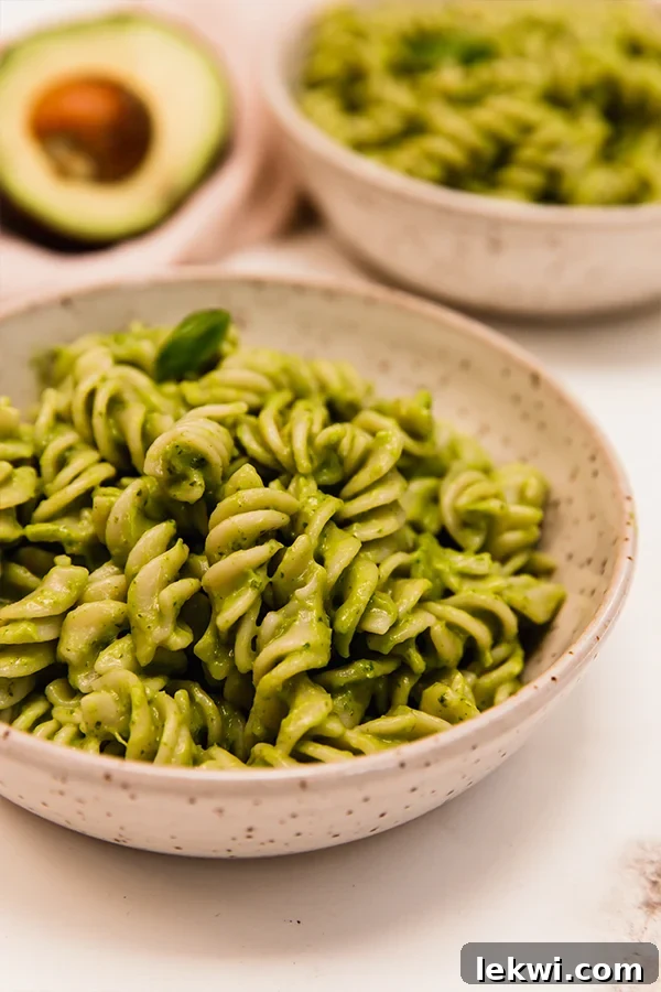 Bowl of creamy avocado pesto pasta, garnished with fresh basil.