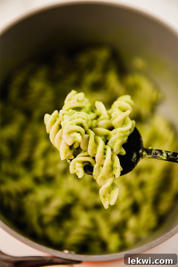 A serving spoon lifting a portion of avocado pesto pasta, showing its creamy texture.