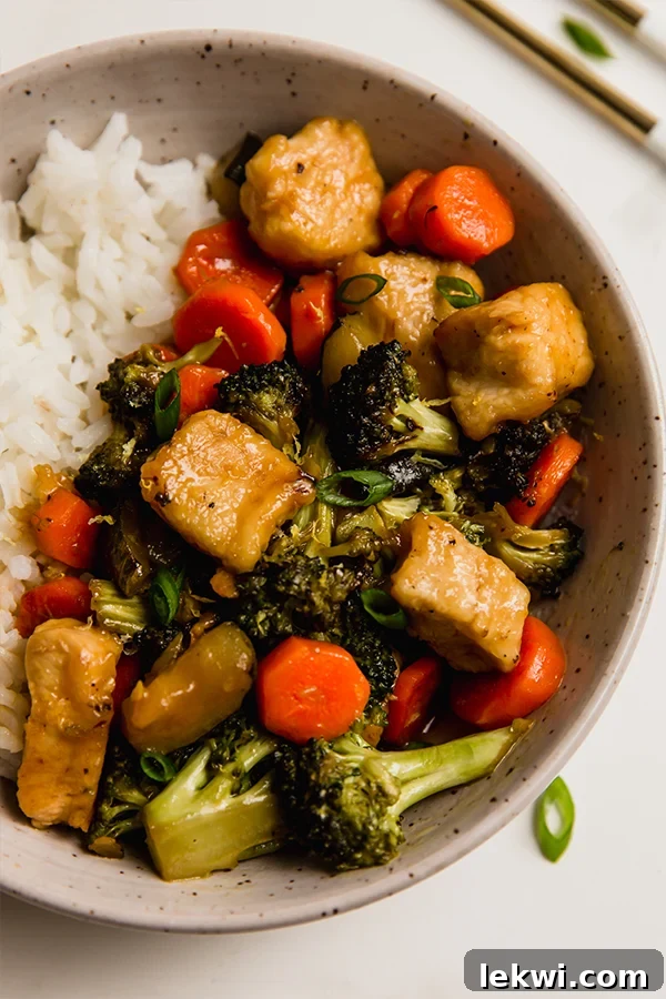 Zesty lemon chicken and colorful vegetable stir fry, served alongside fluffy white rice in a rustic bowl.