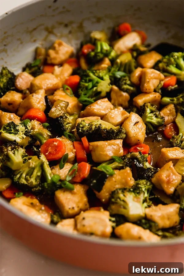 The finished lemon chicken and vegetable stir fry is simmering in a pan, coated in a luscious, thick sauce.