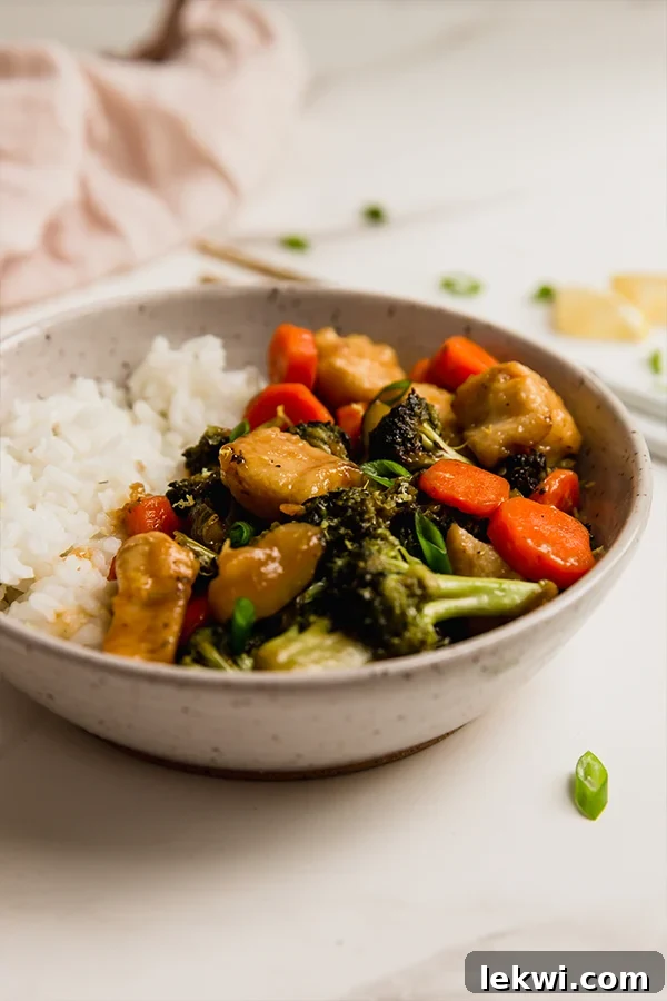 A beautifully presented bowl filled with white rice and a generous serving of lemon chicken and vegetable stir fry, garnished with green onions.