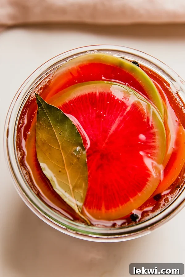 Thin slices of watermelon radish in liquid topped with a bay leaf.