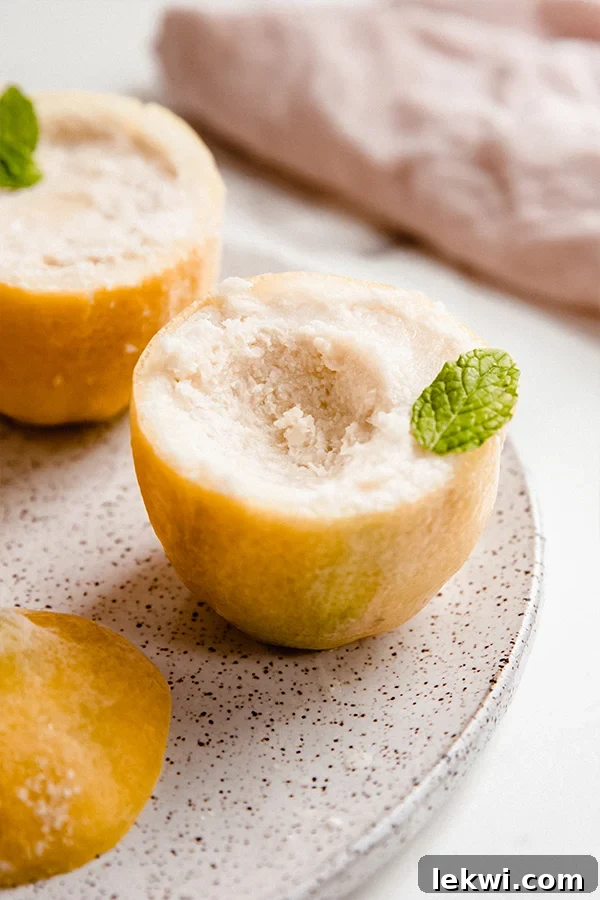 Bright yellow lemon sorbet in natural lemon rinds on a white plate, garnished with fresh mint leaves.