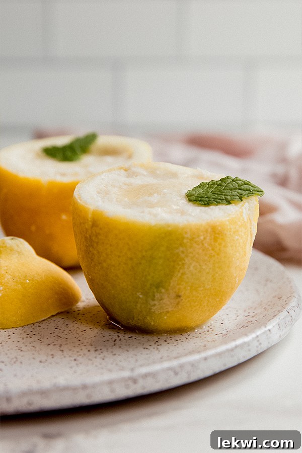 Two beautifully presented lemon sorbet cups, served in real lemon rinds and garnished with fresh mint, resting on a small white plate.