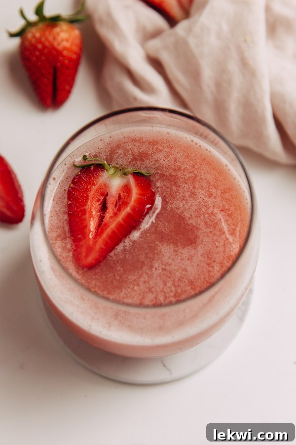 A close-up shot of a glass of frose, adorned with a fresh strawberry slice, resting on a wooden surface, highlighting its frosty texture and inviting appeal.