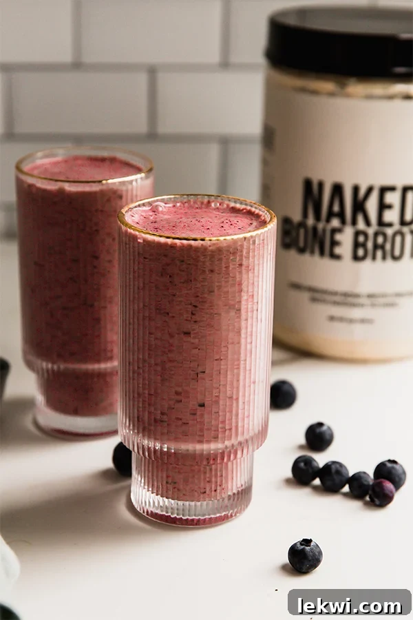 Power berry smoothie in a glass with a container of Naked Bone Broth protein powder in the background.