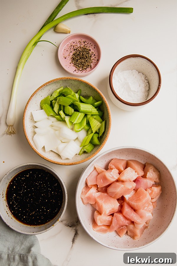 A vibrant flat lay of fresh ingredients laid out for Black Pepper Chicken stir-fry, including bright green onions, crisp celery stalks, whole garlic cloves, and avocado oil, ready for preparation.