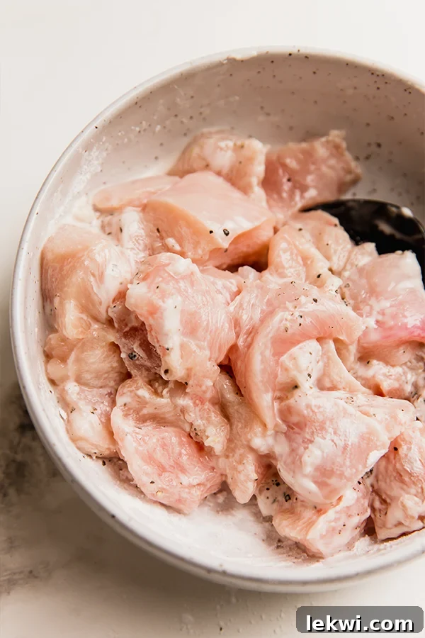 Close-up shot of cubed chicken breast coated in arrowroot powder and seasoned with salt and pepper in a mixing bowl, ready for cooking.