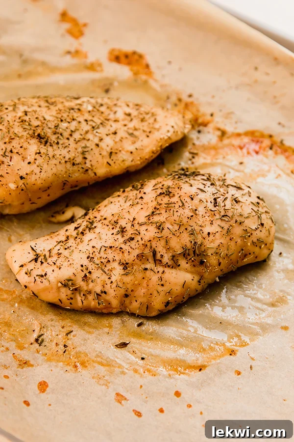 Seasoned chicken breasts on a baking sheet lined with parchment paper, ready for the oven.