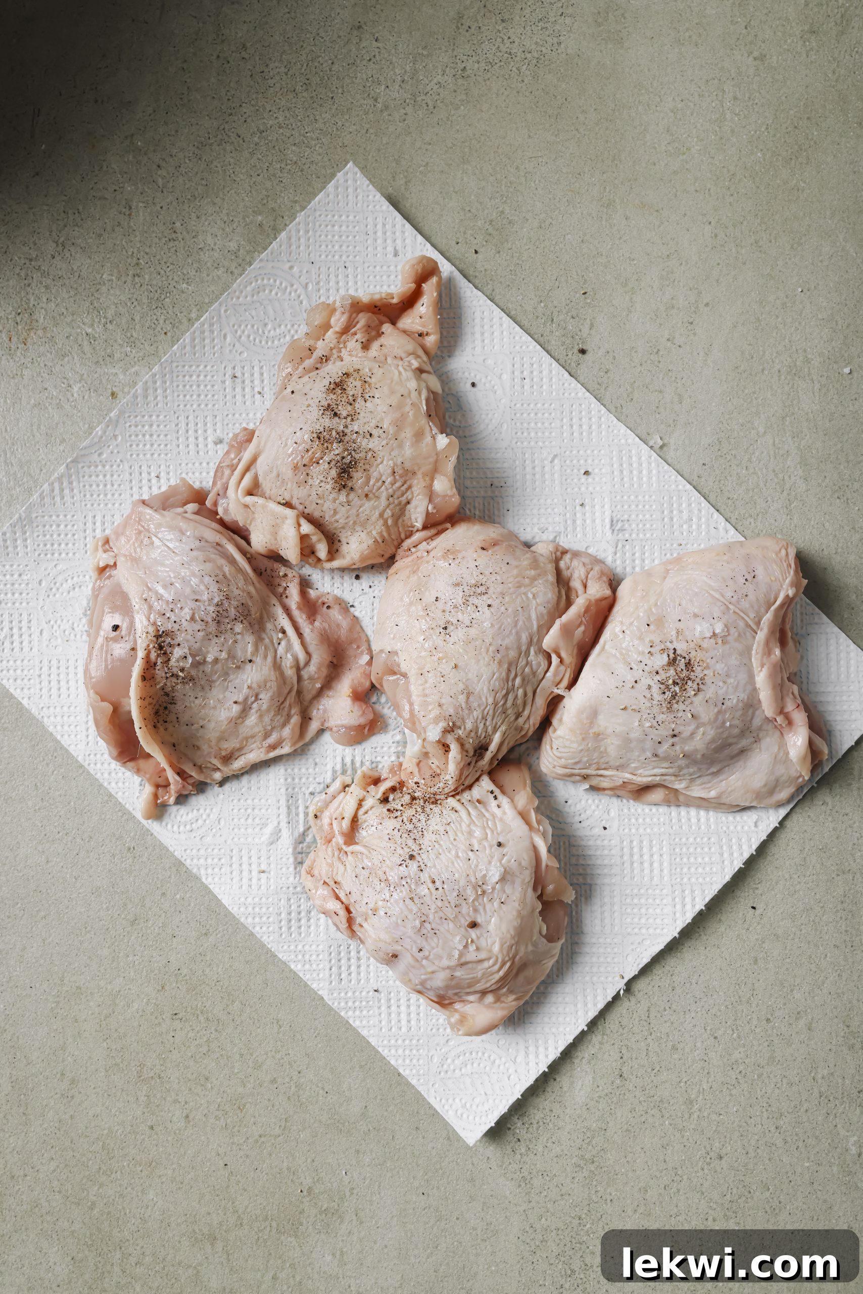 Seasoned raw chicken thighs on a paper towel, ready for searing.