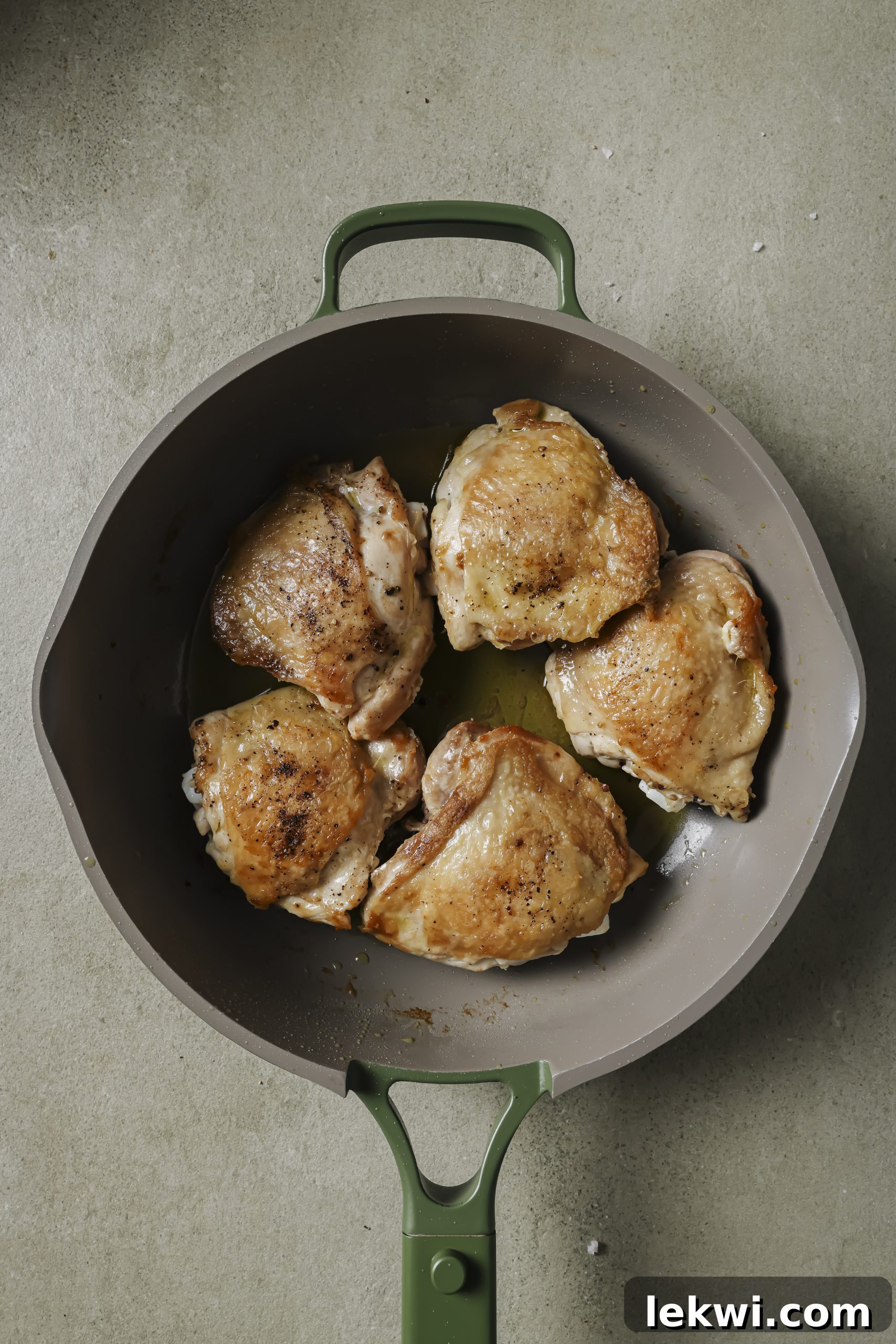 Chicken thighs searing in a pan, skin side down, developing a golden-brown crisp.