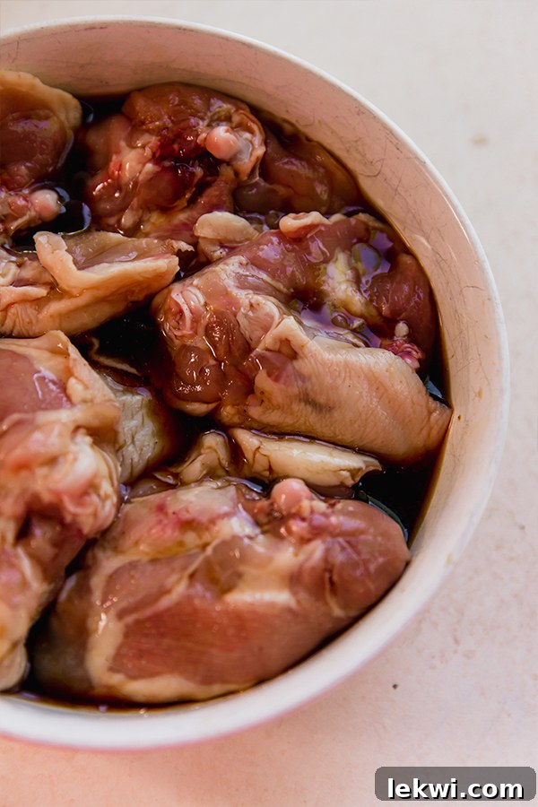 Chicken thighs marinating in a savory Asian sauce in a glass bowl.