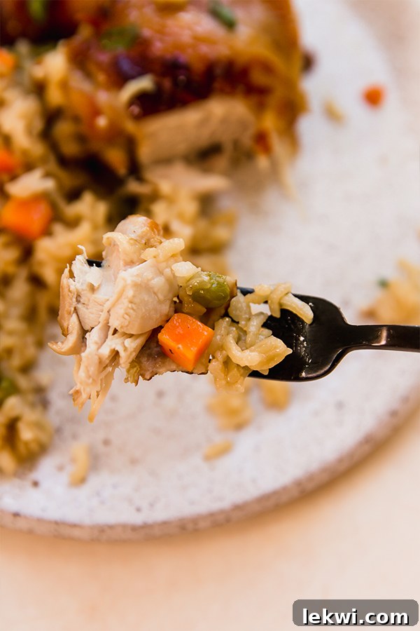 A fork holding a piece of tender Asian-inspired chicken with fragrant rice and peas.
