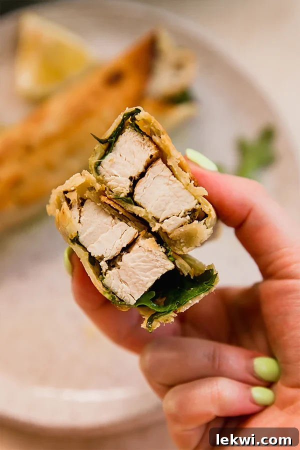 A golden-brown, crispy gluten-free chicken pesto wrap cut in half, revealing the vibrant filling inside, presented on a white plate.