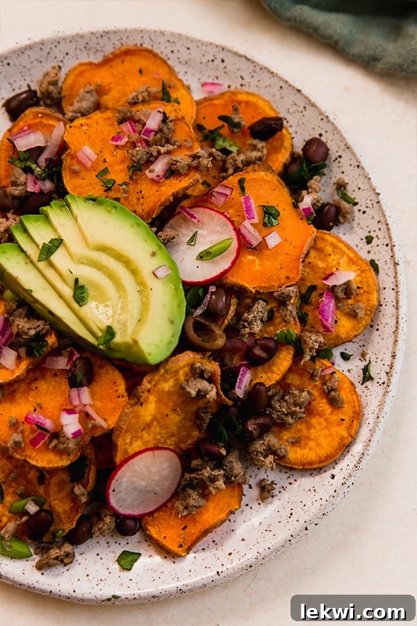 Sweet potato nachos on a plate, garnished with fresh toppings like avocado, radishes, and cilantro.