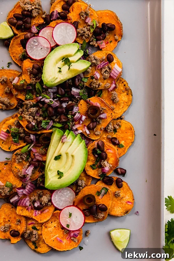 A baking sheet laden with freshly assembled sweet potato nachos, topped with beef and fresh vegetables.