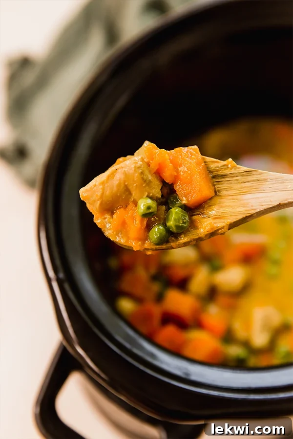 A close-up of a spoonful of Slow Cooker Turmeric Chicken Curry, showcasing the tender chicken, vibrant vegetables, and rich, creamy sauce.