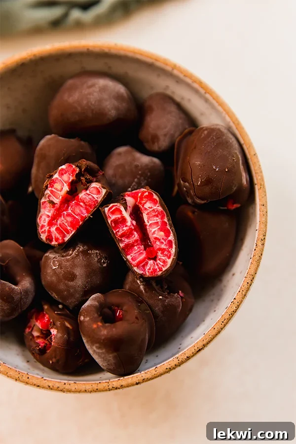 A bowl overflowing with perfectly layered chocolate covered frozen raspberries, showcasing their appealing dual-chocolate coating and vibrant red centers.