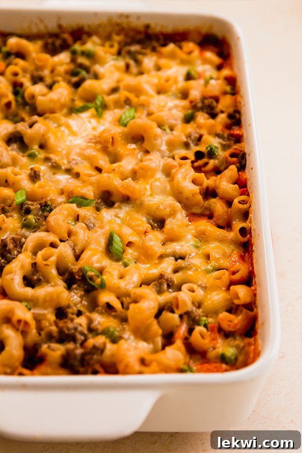 A golden brown, bubbly sloppy joe pasta casserole in a baking dish, garnished with fresh green onions.