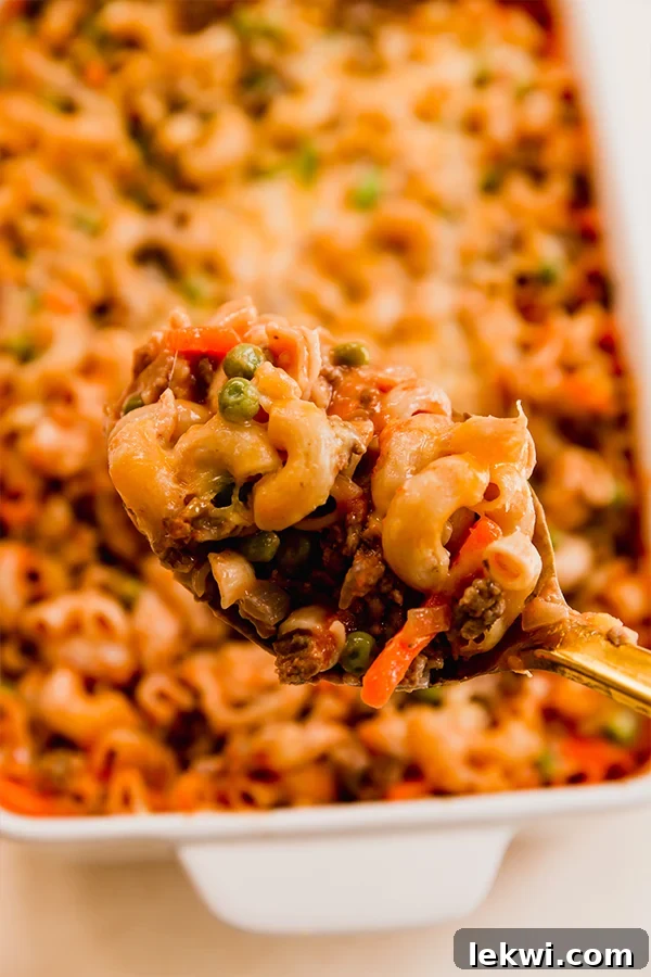 A spoon scooping a portion of sloppy joe pasta casserole from the baking dish.
